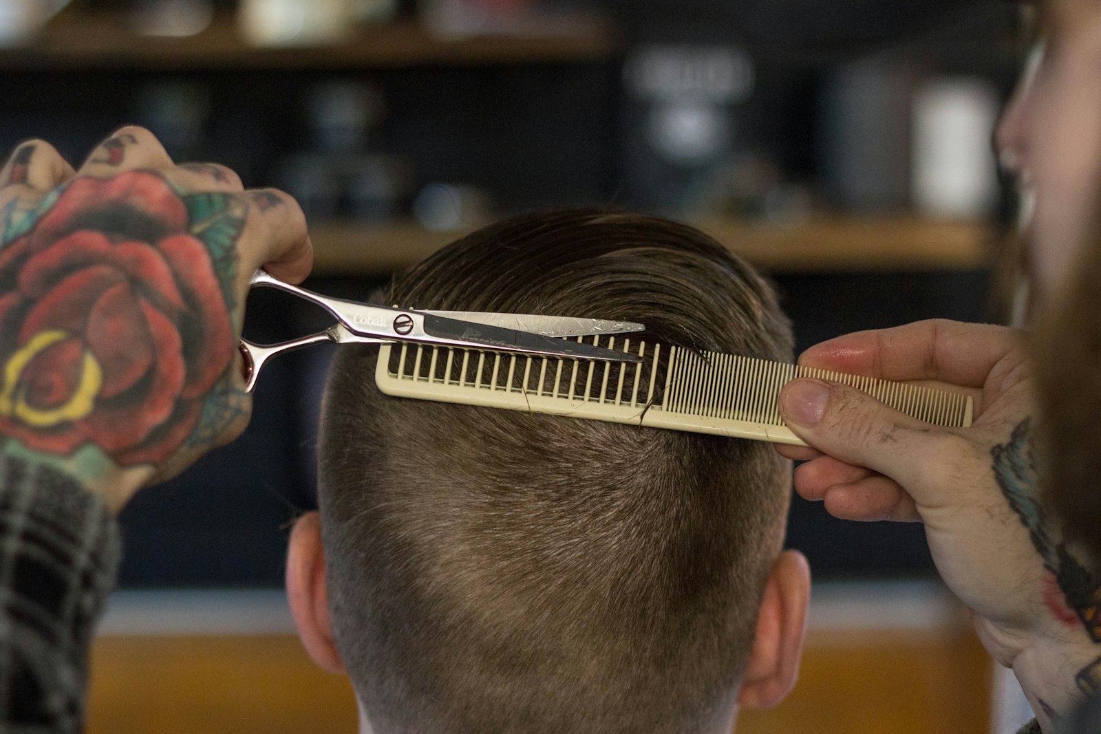 Un coiffeur coupe les cheveux au ciseau, peigne en main, en gros plan.