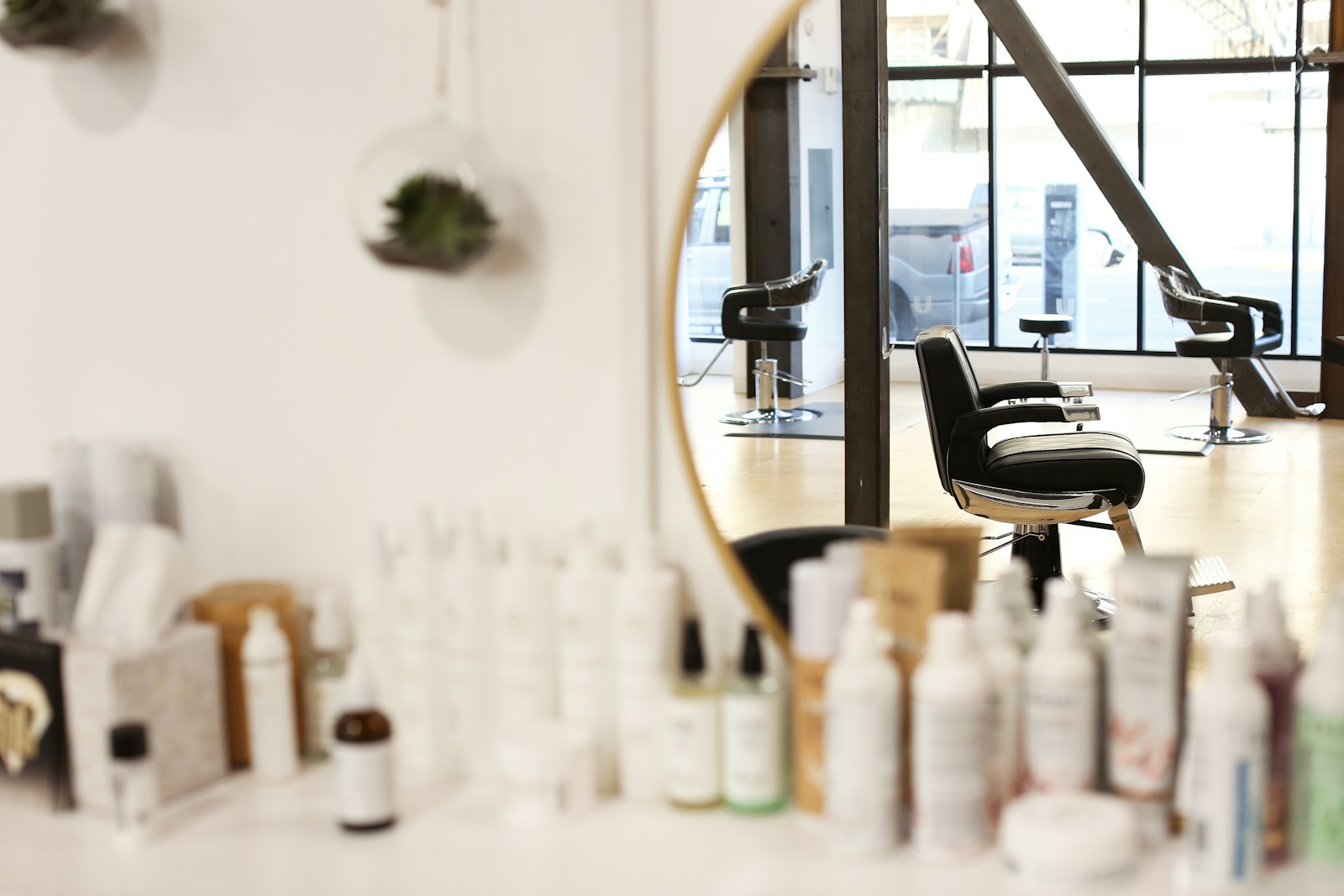Salon vu à travers un miroir rond, avec les fauteuils et les produits capillaires en arrière-plan.