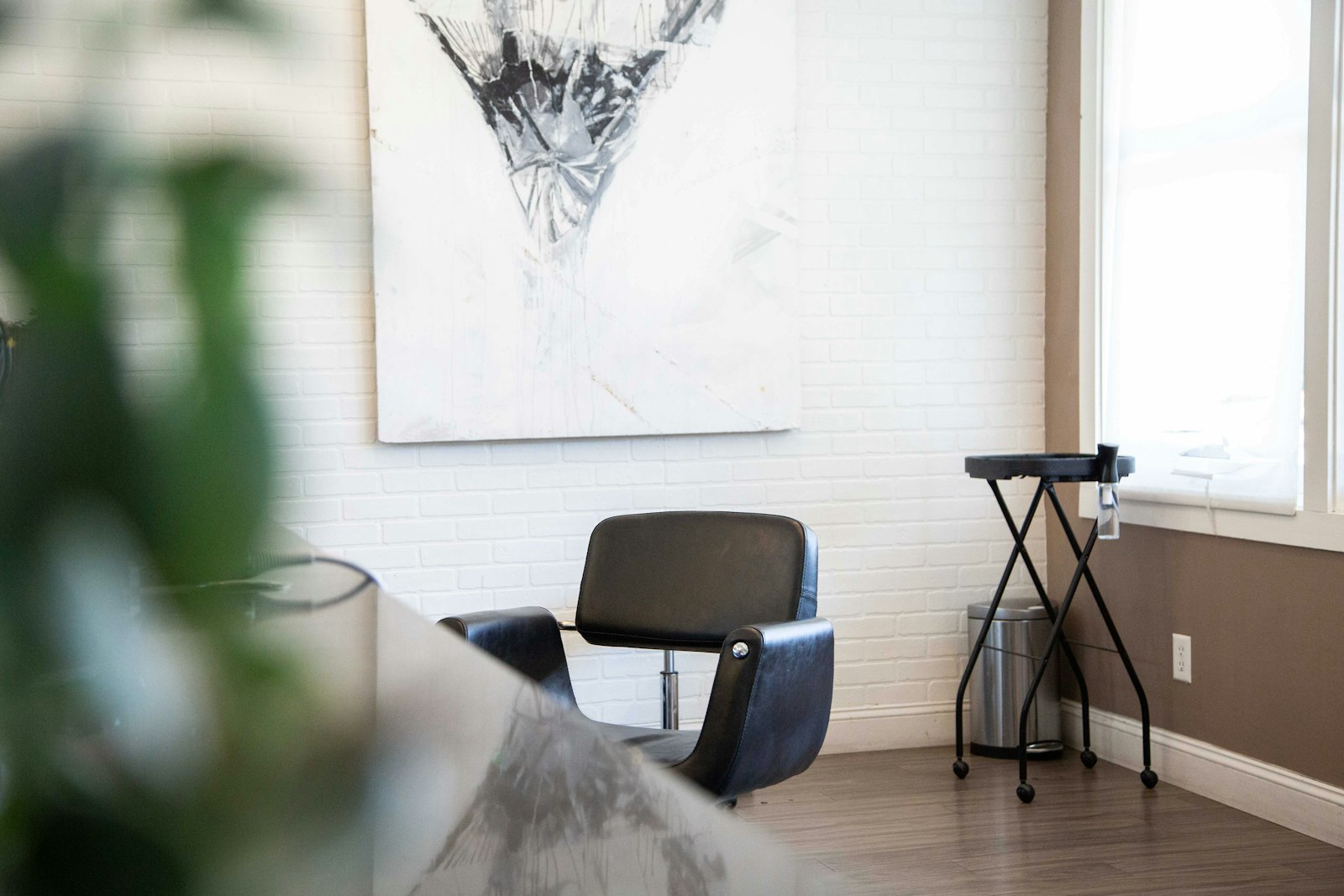 Fauteuil de coiffure devant un mur de brique blanche, sous un tableau abstrait.