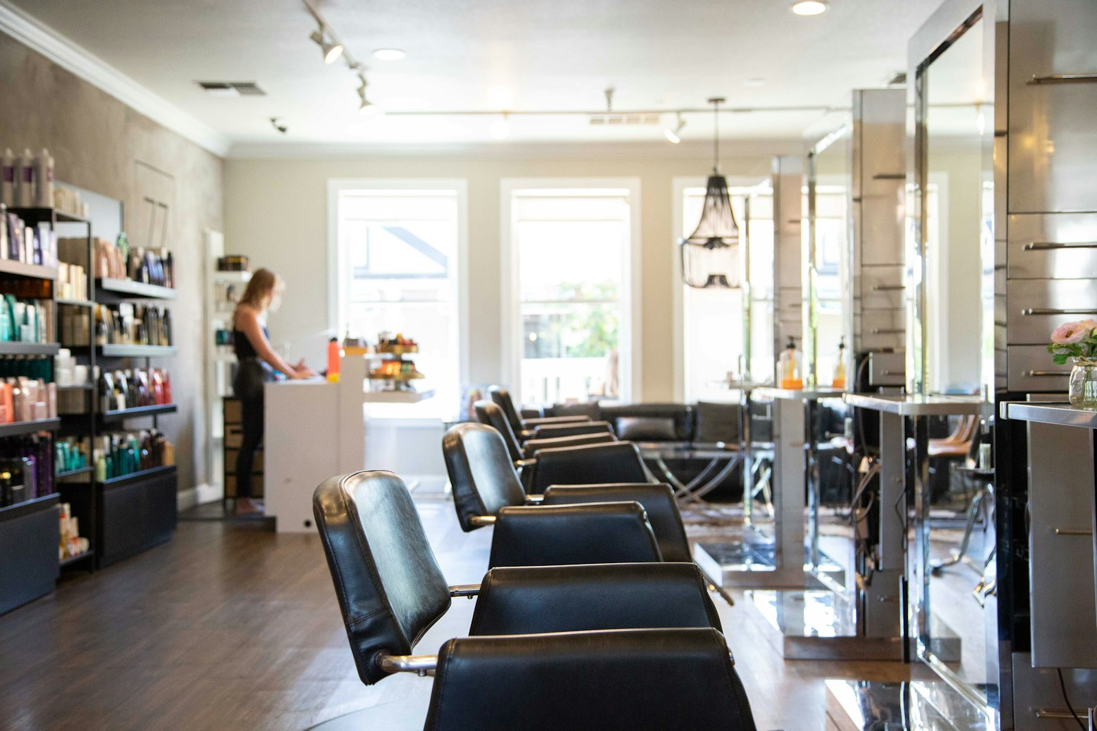 Rangée de fauteuils de coiffure face aux miroirs, dans un salon lumineux aux étagères garnies de produits.