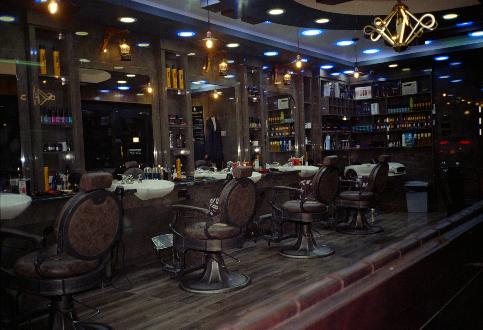 Salon de coiffure façon barbershop, fauteuils en cuir et étagères de produits sous un éclairage tamisé.