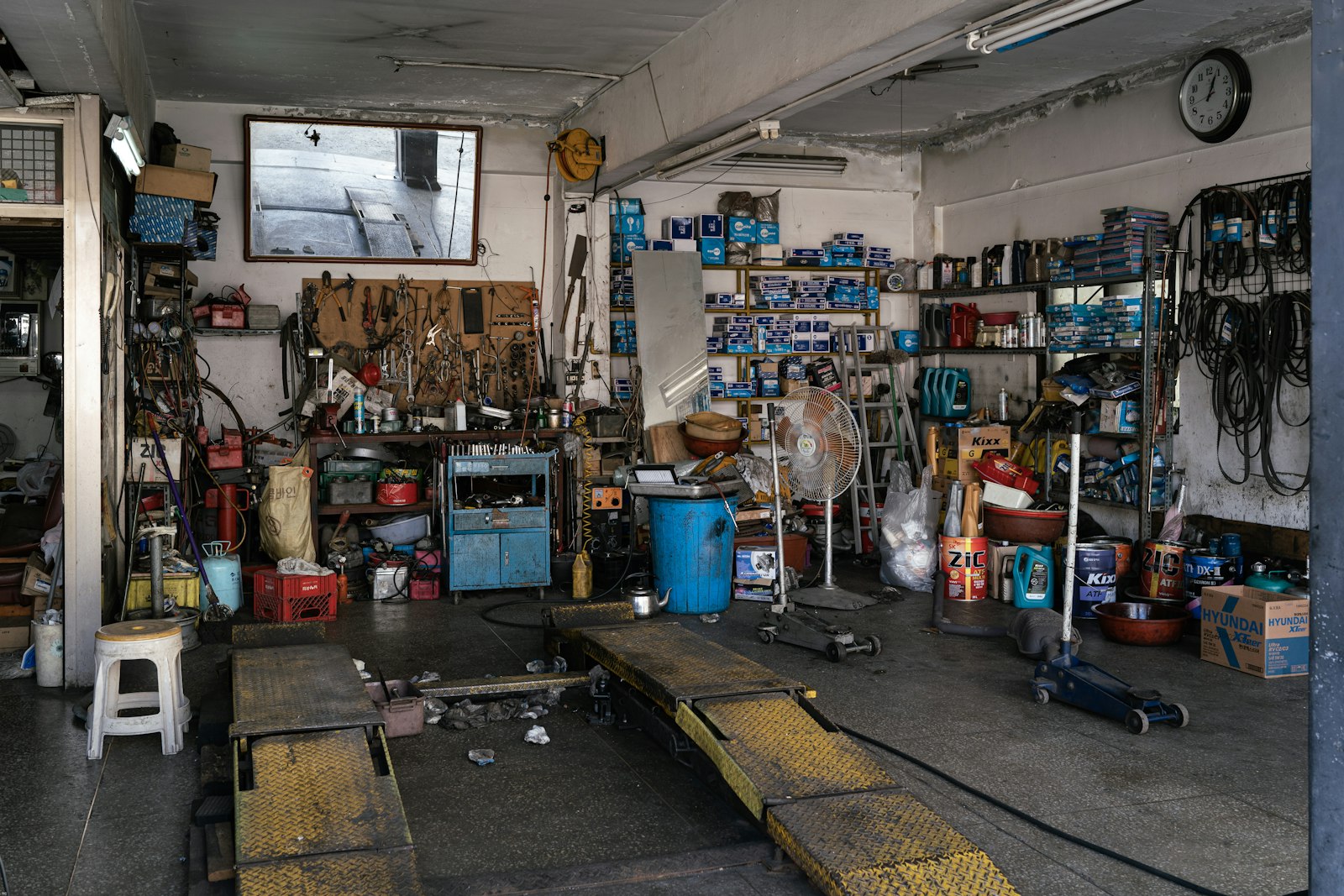 Atelier de mécanique bien fourni, étagères de pièces et de bidons, rampe de levage au sol.