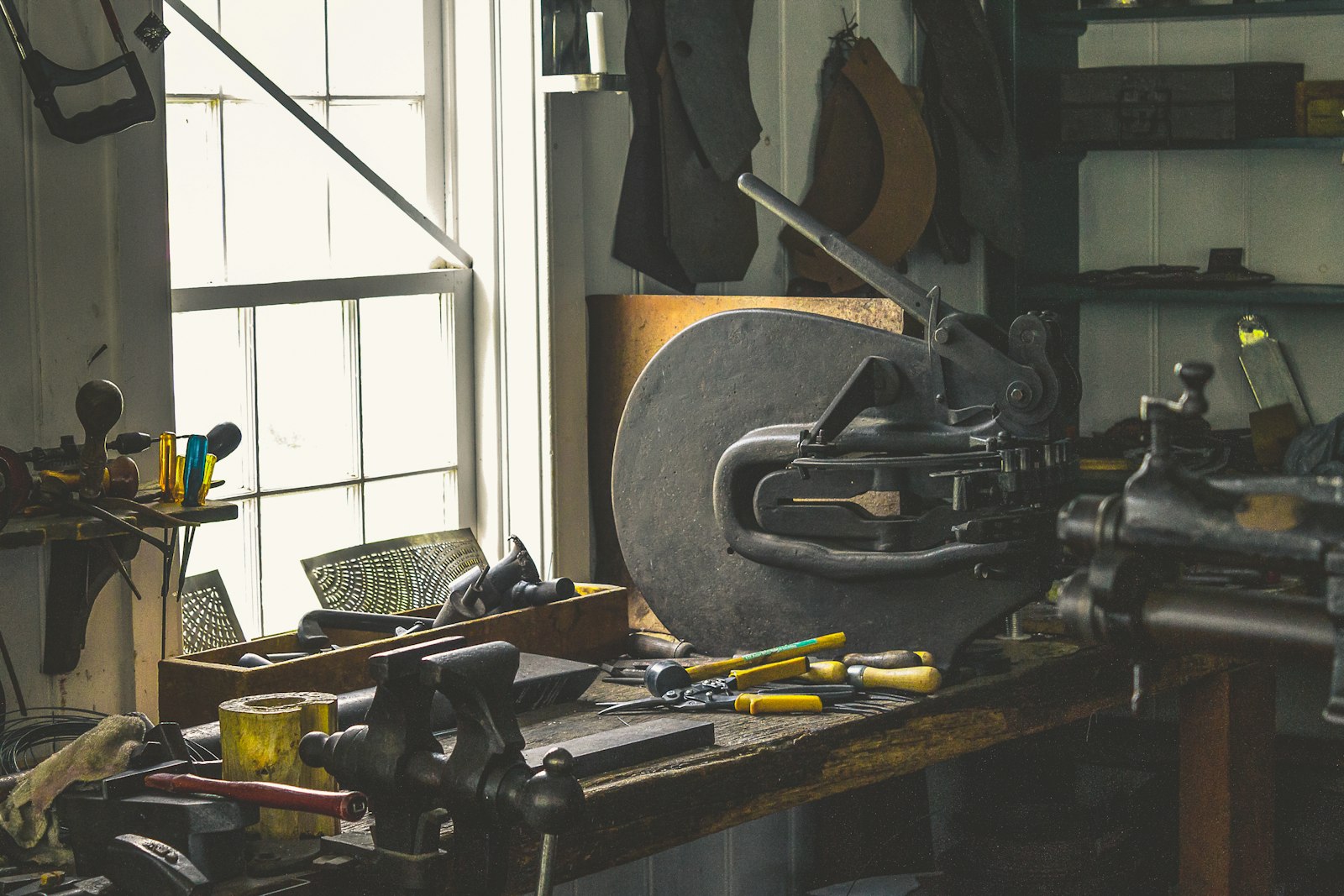 Établi d'atelier garni d'outils anciens, sous une fenêtre éclairant le plan de travail.