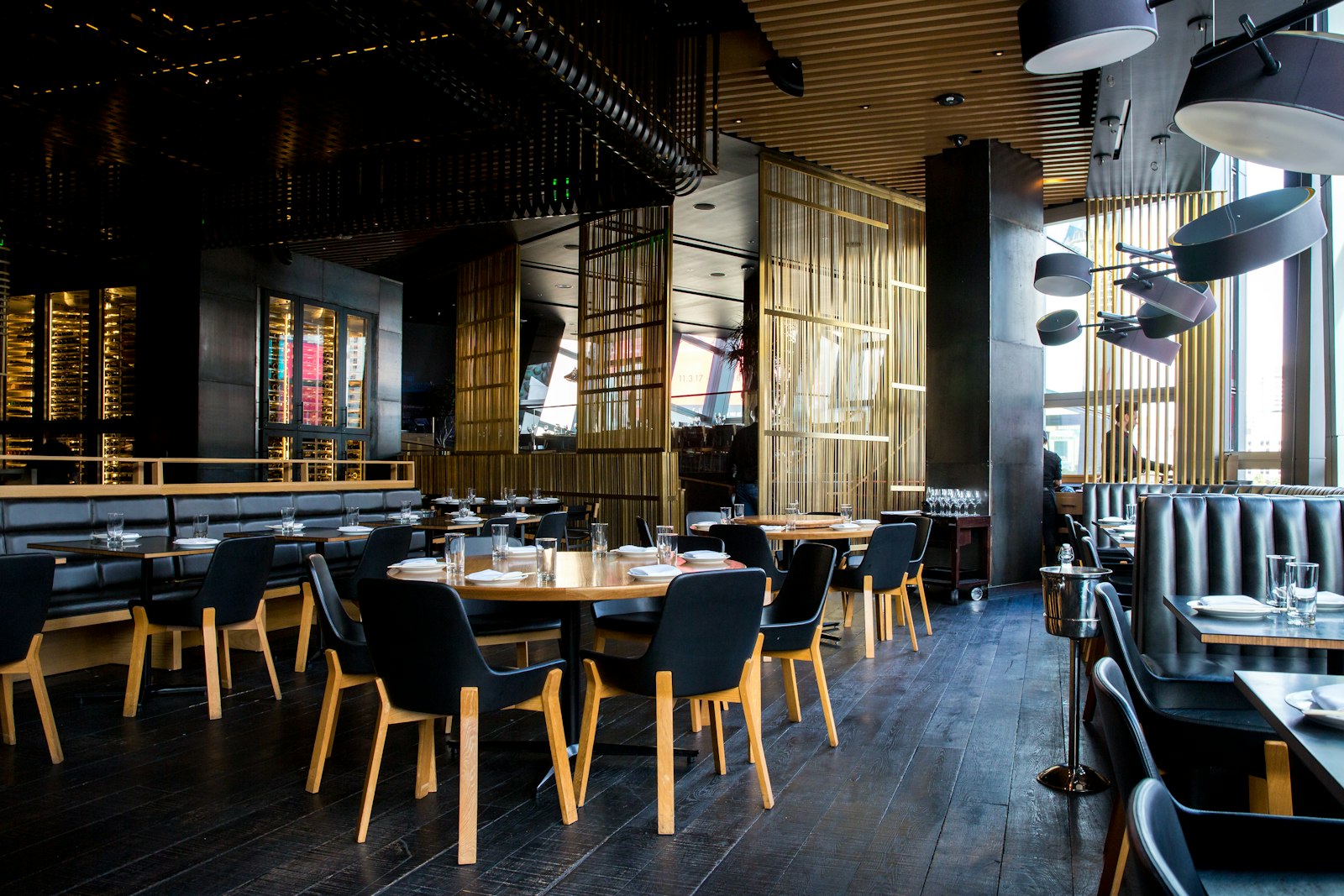 Salle du restaurant aux tables rondes dressées, sous des suspensions dorées.