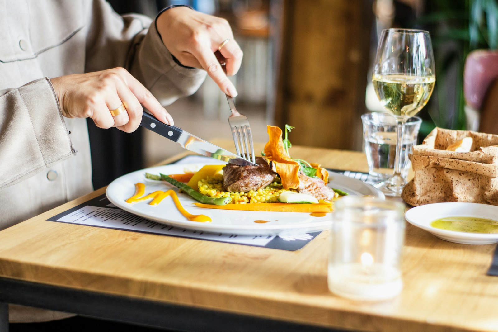 Assiette de viande accompagnée de légumes et de chips de patate douce, servie avec un verre de vin blanc.