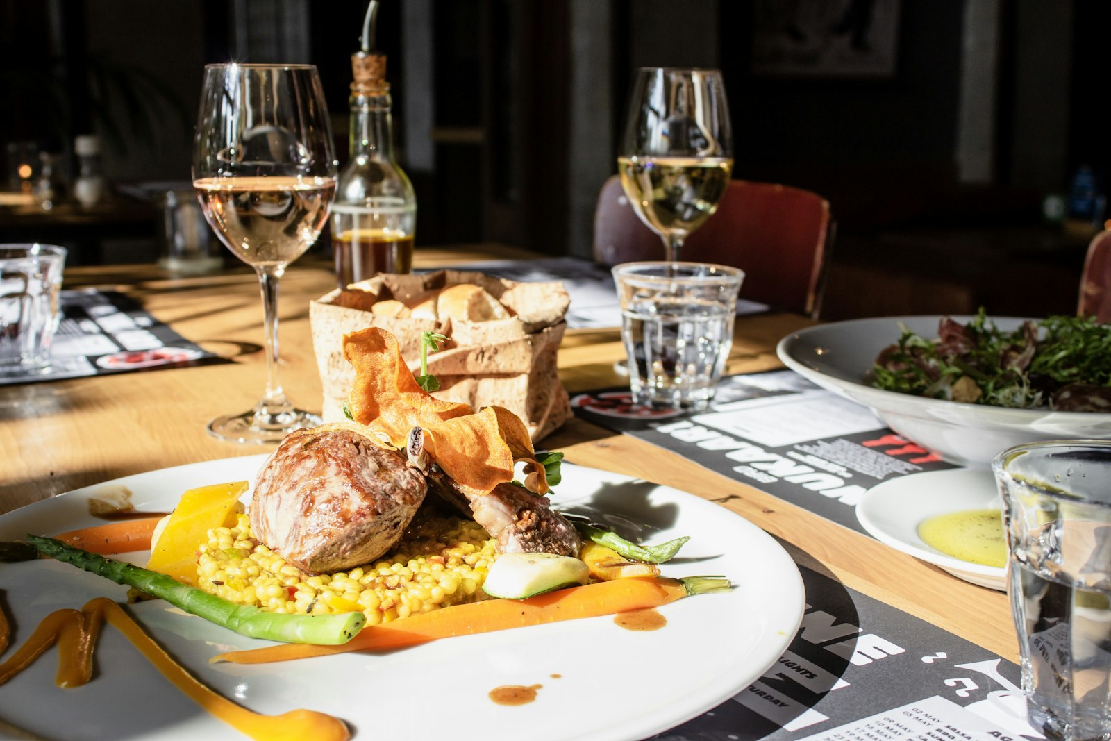 Plat de viande sur lit de boulgour, entouré de légumes de saison et d'un panier de pain.