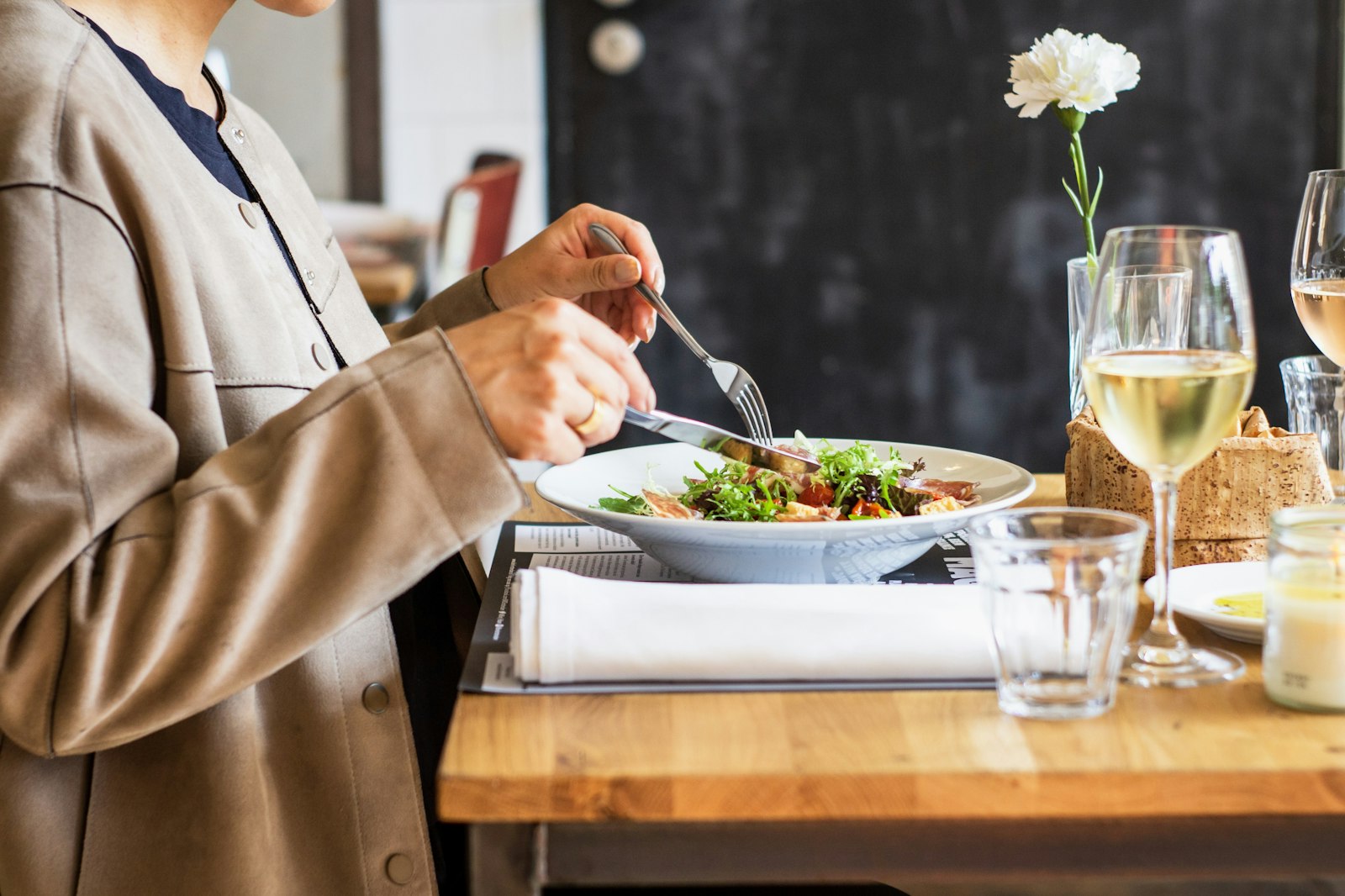 Salade composée servie dans une assiette creuse, accompagnée d'un verre de vin blanc et d'une fleur en table.